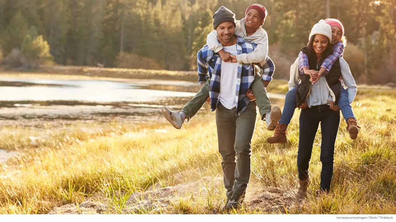 Parents giving children piggyback ride on walk by lake