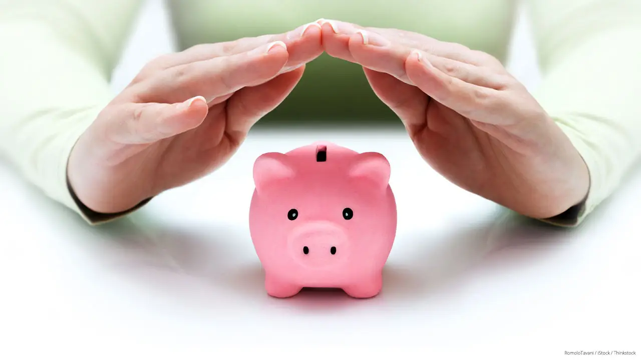 Two hands covering a small pink piggy bank to protect it